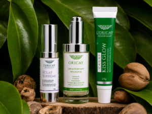 Aceite de Cacay, Eclat Supreme y Kiss Glow de L'ORICAY sobre madera rodeados de nueces y hojas de Cacay